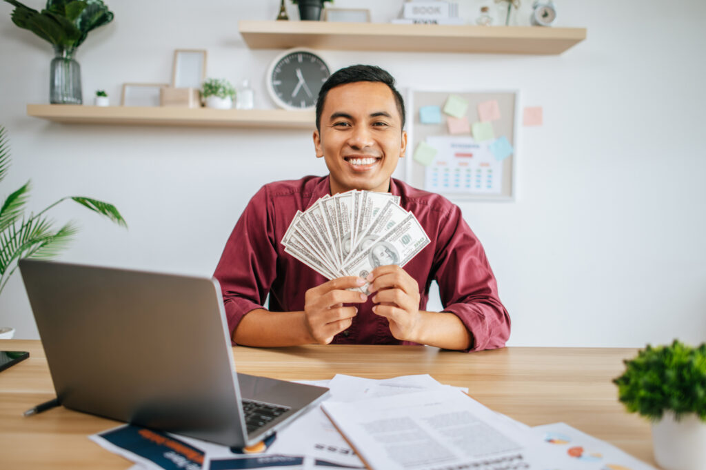 Image de un hombre en su escritorio junto a su laptop, mostrando el dinero recibido de un préstamo